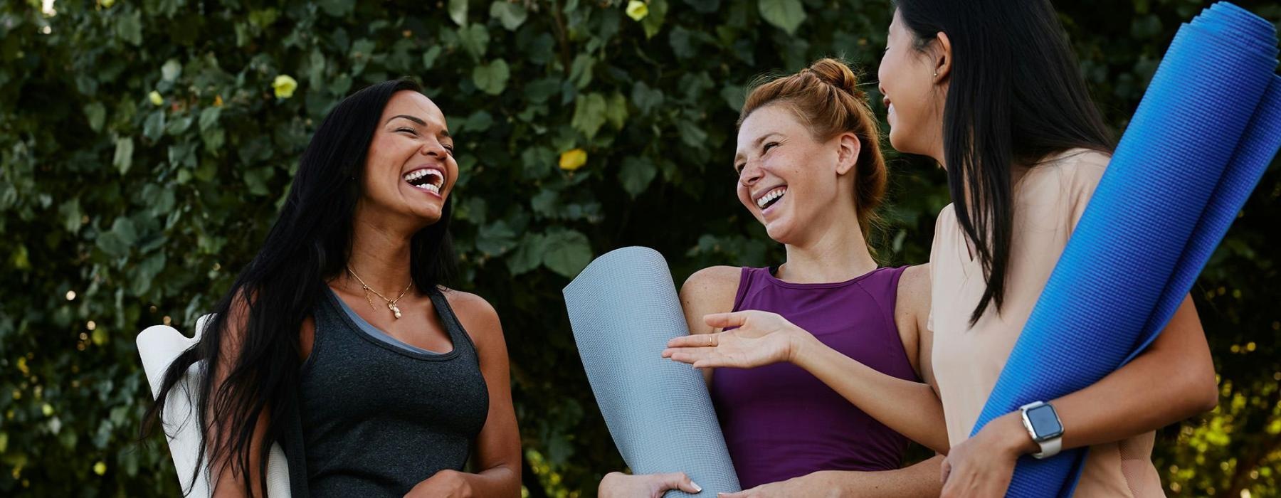 A group of women holding yoga mats and laughing.